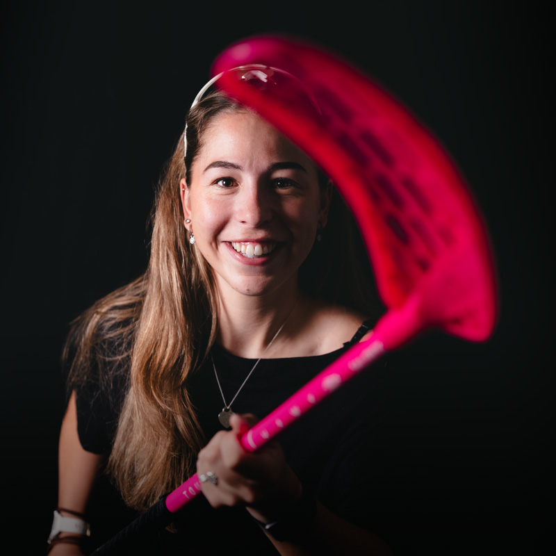 Junge Frau mit einem pinken Unihockey-Schläger vor schwarzem Hintergrund